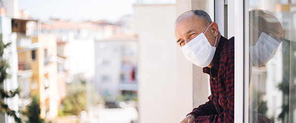 Senior man in medical mask on window breathing fresh air from quarantine.