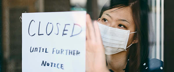Woman wearing mask posts sign on door that says Closed Unitil Further Notice.